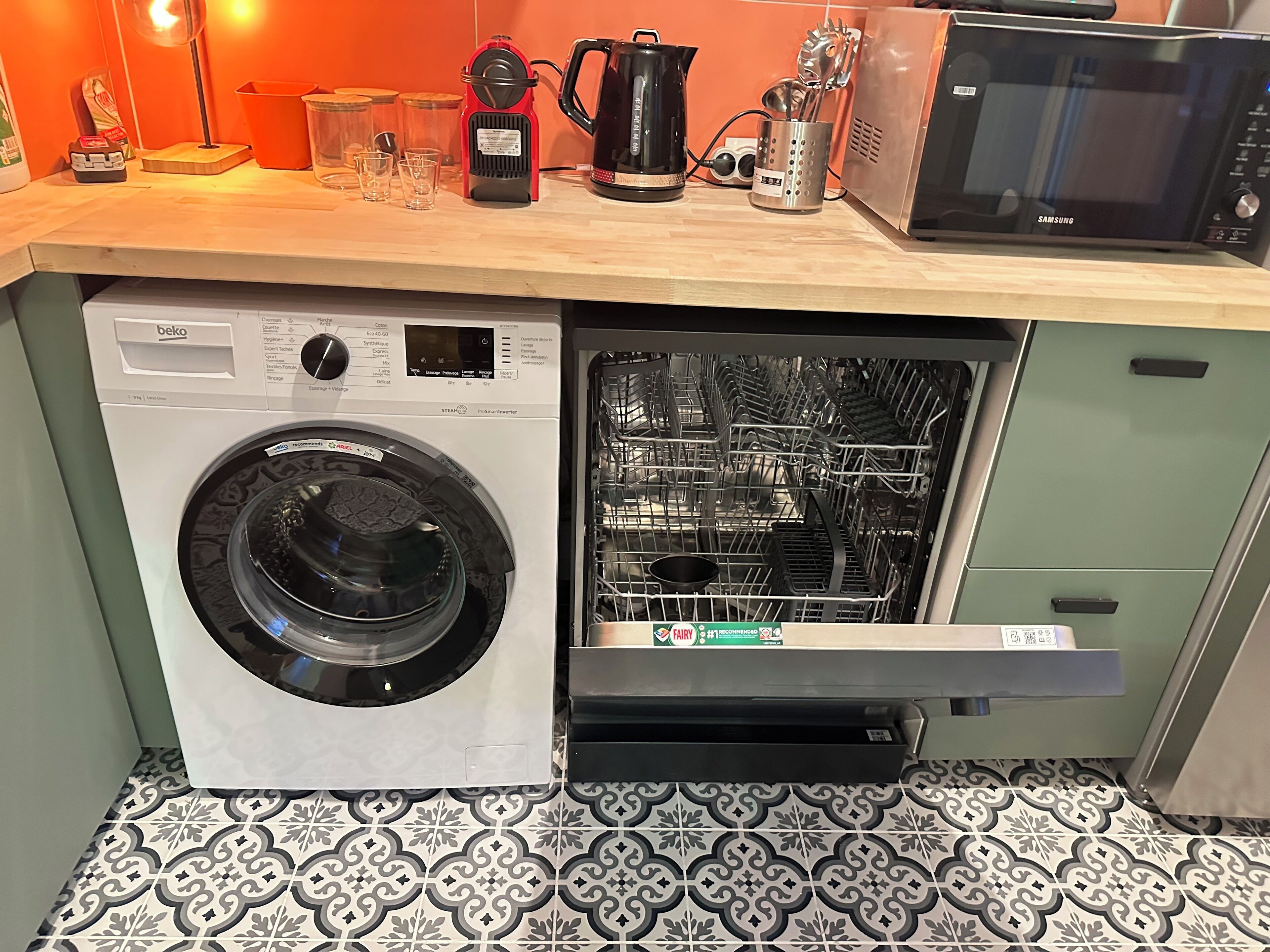 Een compacte keuken met een ingebouwde wasmachine en droger, een magnetron en een koffiezetapparaat op het aanrecht.