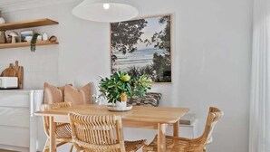 A modern kitchen with a wooden dining table, wicker chairs, and a potted plant.