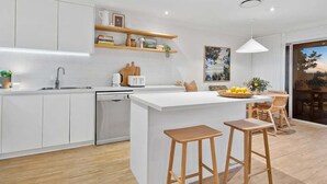 A modern kitchen with white cabinetry, a central island with stools, a dishwasher, and a dining area with a table and chairs.