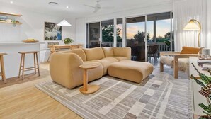 A modern living room with a sectional sofa, a dining area, and a kitchen in the background.