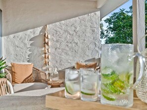 A cozy outdoor seating area with a wicker sofa, a wooden table with drinks, and a textured wall.