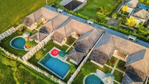 An aerial view of a resort with multiple swimming pools, each surrounded by lounge areas and covered by thatched roofs. - Sunrise Terrace Ubud Vila by Nagisa Bali (Ubud)