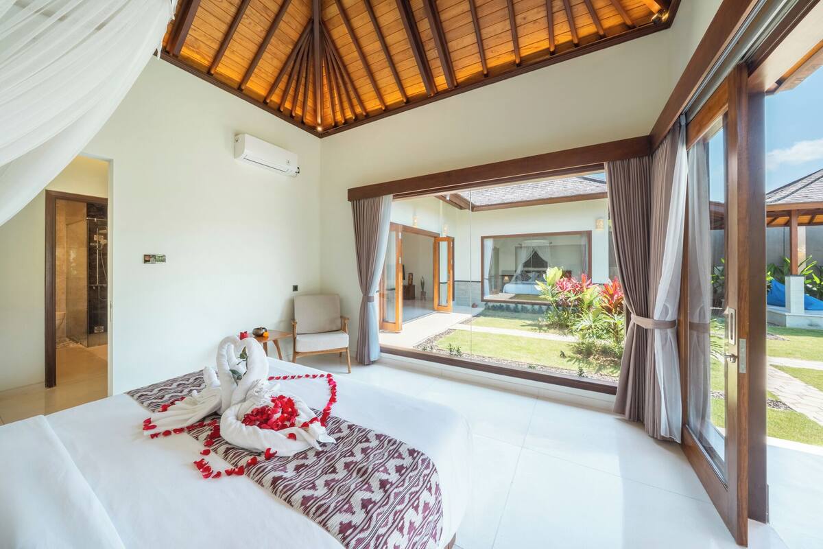 A bedroom with a large bed, a shower, and a view of the garden.
