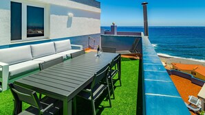 A rooftop terrace with a dining table, chairs, and a sofa, overlooking the ocean.