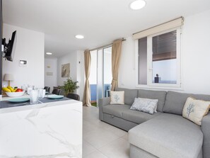 A modern living room with a grey sofa, a dining area with a table set for two, and a large window with curtains.