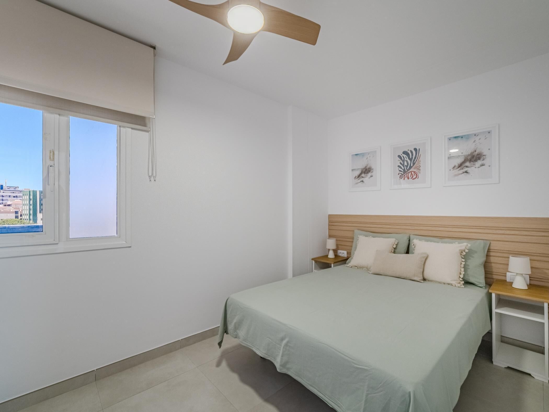 A bedroom with a bed, a ceiling fan, a window, and artwork on the wall.