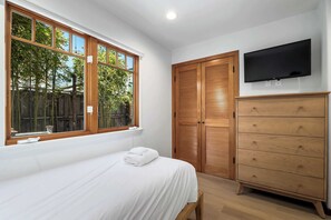 A bedroom with a large window, wooden wardrobe, and a TV on the wall.
