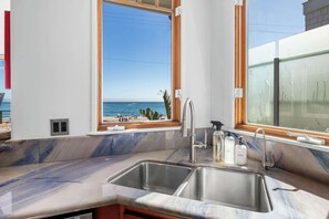 A kitchen with a large window overlooking a beach, a sink, and a countertop.