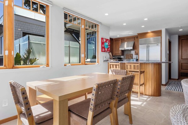 A modern kitchen with wooden cabinets, a stainless steel refrigerator, and a dining area with a wooden table and chairs.