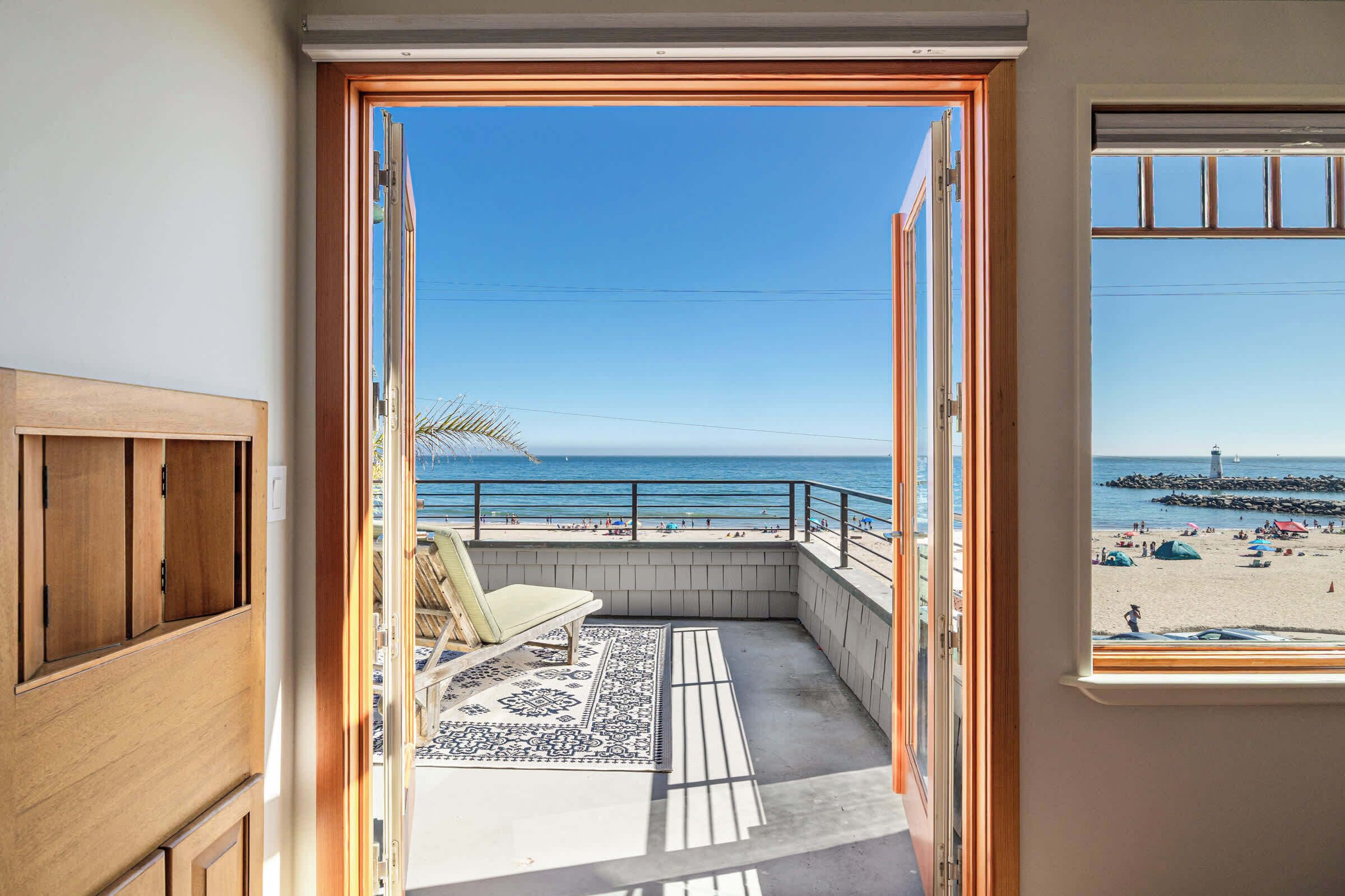 A balcony with a view of the beach, a chair, and a patterned rug.