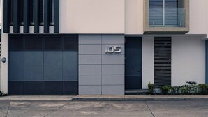 Um edifício moderno com uma grande porta de garagem, uma placa com o número '105' e uma janela com moldura de metal.