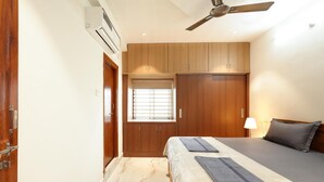 A bedroom with a bed, a ceiling fan, wooden cabinets, a window with blinds, and a marble floor. - Enjoyable building with AC in vibrant Hyderabad (Hyderabad)