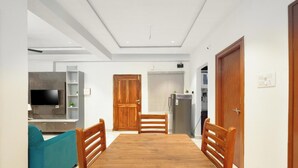 A modern apartment with a wooden dining table, two wooden chairs, a teal sofa, a kitchen area with a refrigerator, and a television. - Enjoyable building with AC in vibrant Hyderabad (Hyderabad)