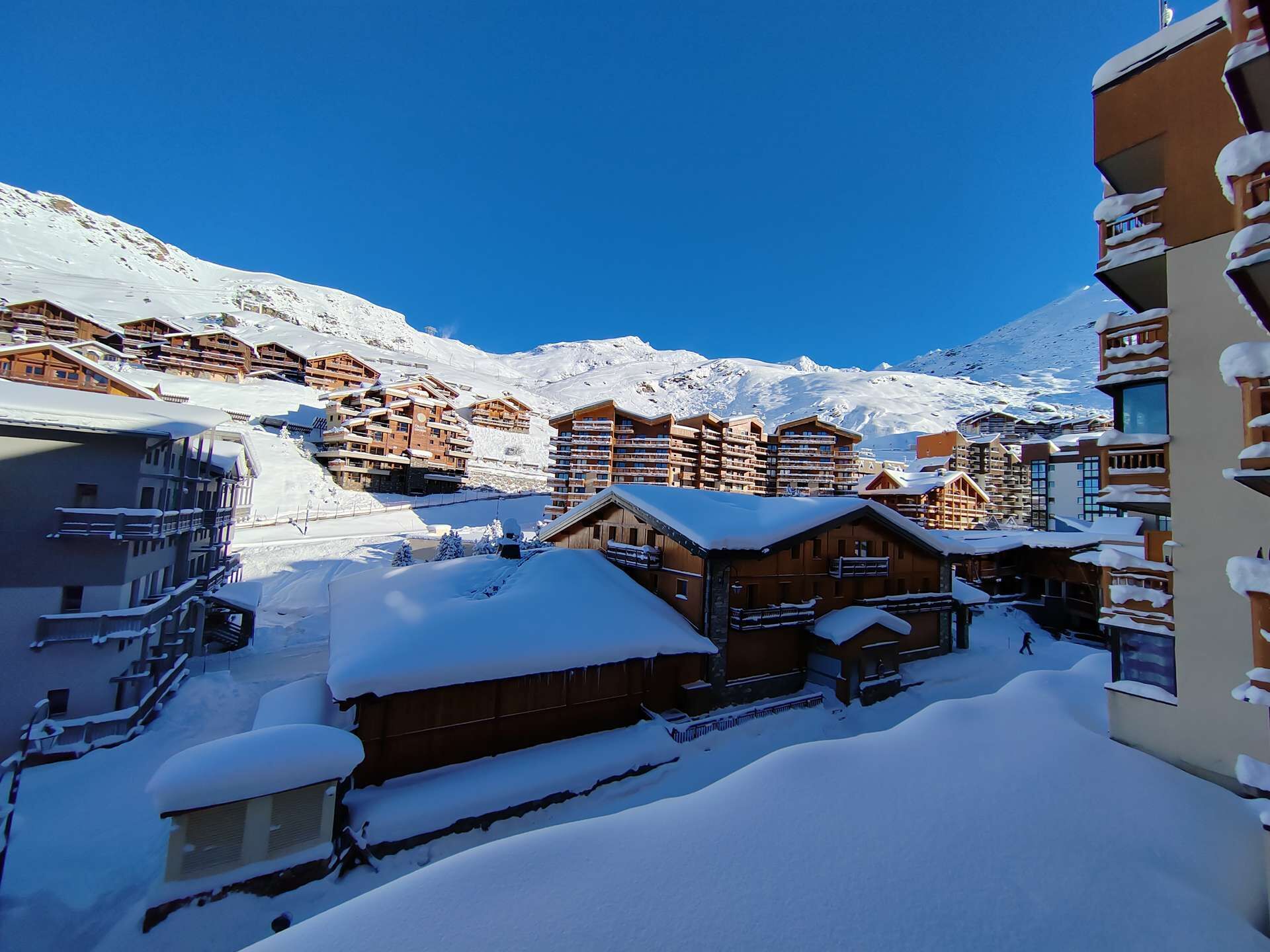 A snow-covered mountain resort with wooden buildings and a clear blue sky.