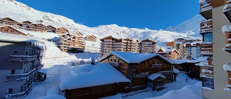 Une station de montagne enneigée, avec des bâtiments en bois et un ciel bleu azur.