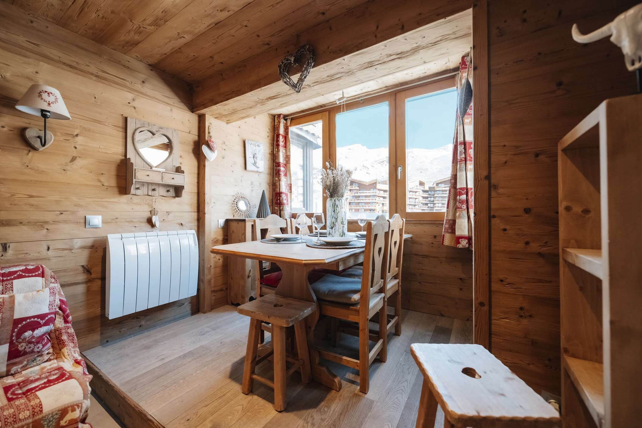 Un intérieur en bois comprenant une table à manger, des chaises, un radiateur et une fenêtre donnant sur des immeubles.