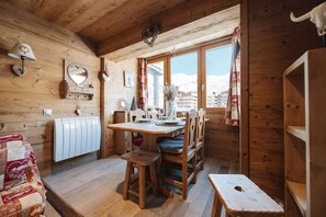 Interior de madera con una mesa de comedor, sillas, un radiador y una ventana que ofrece vistas a edificios.