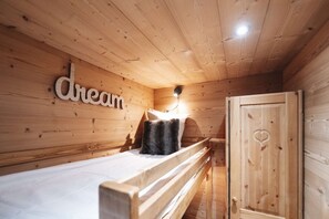 Una habitación de cabaña de madera con literas, una lámpara fijada a la pared y una puerta con un recorte en forma de corazón.