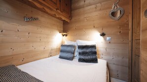 Quarto de cabana de madeira com uma cama, duas almofadas, uma luminária na parede e uma decoração em formato de coração.