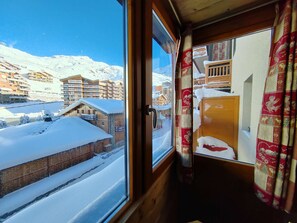 Vista desde una ventana de un balneario nevado en la montaña, con edificios de madera y cielo despejado.