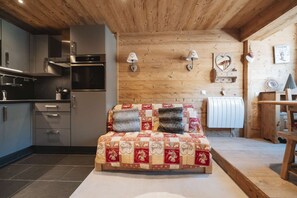 Ein Schlafzimmer mit Holzbalkendecke, einem Bett mit Patchwork-Quilt, einer Küche mit modernen Geräten und einer Holzwand mit Dekoration.