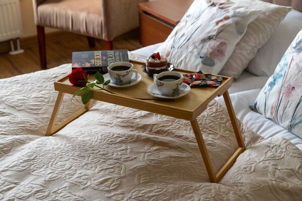 A bed with a wooden tray holding a book, two cups of coffee, and a dessert.
