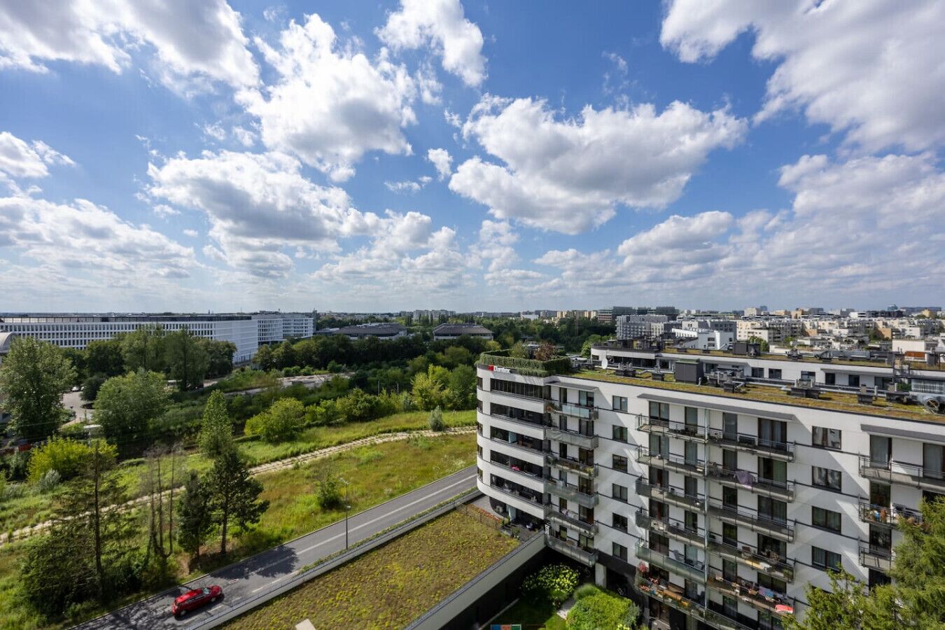 Un immeuble d’appartements moderne doté de nombreux balcons, d’un toit végétalisé et offrant une vue sur un paysage urbain composé de différents bâtiments.