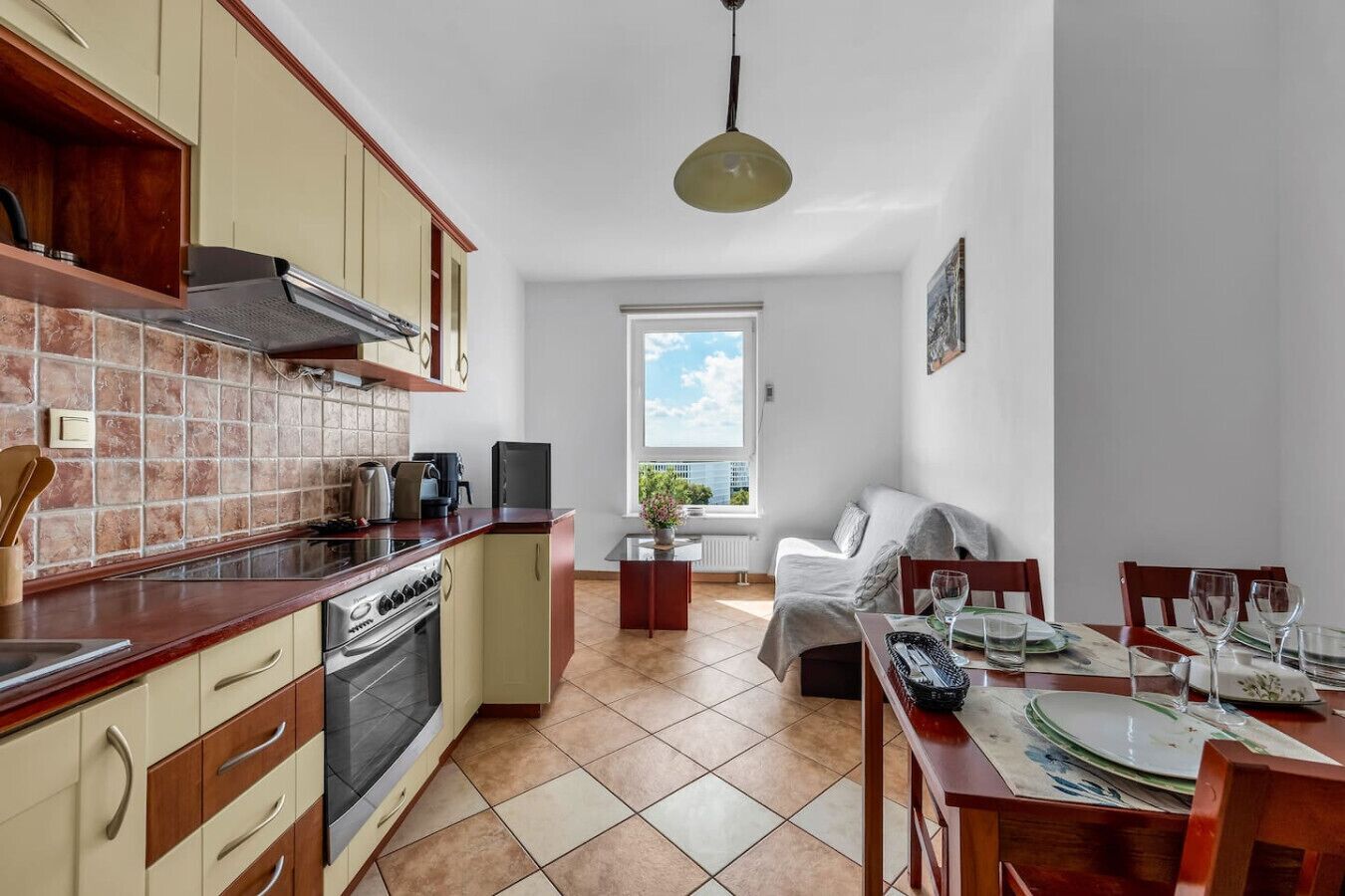 Une cuisine compacte équipée d’une cuisinière, d’un four et d’appareils électroménagers modernes. On y trouve un coin repas avec une table pour deux personnes, ainsi qu’une fenêtre donnant sur l’extérieur.