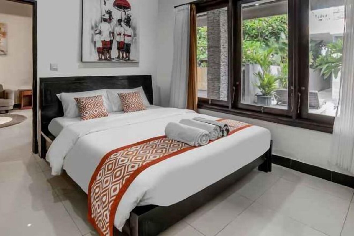 Une chambre d’hôtel avec un grand lit, une tête de lit, une fenêtre avec des rideaux et un tableau au mur.