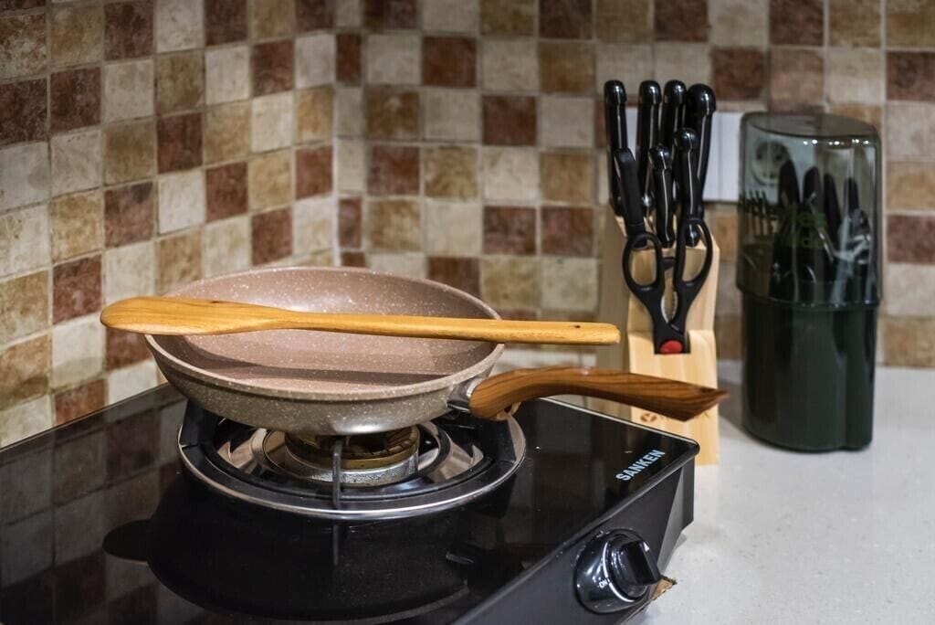 A gas stove with a frying pan on it, a wooden spatula, and a knife block with knives.