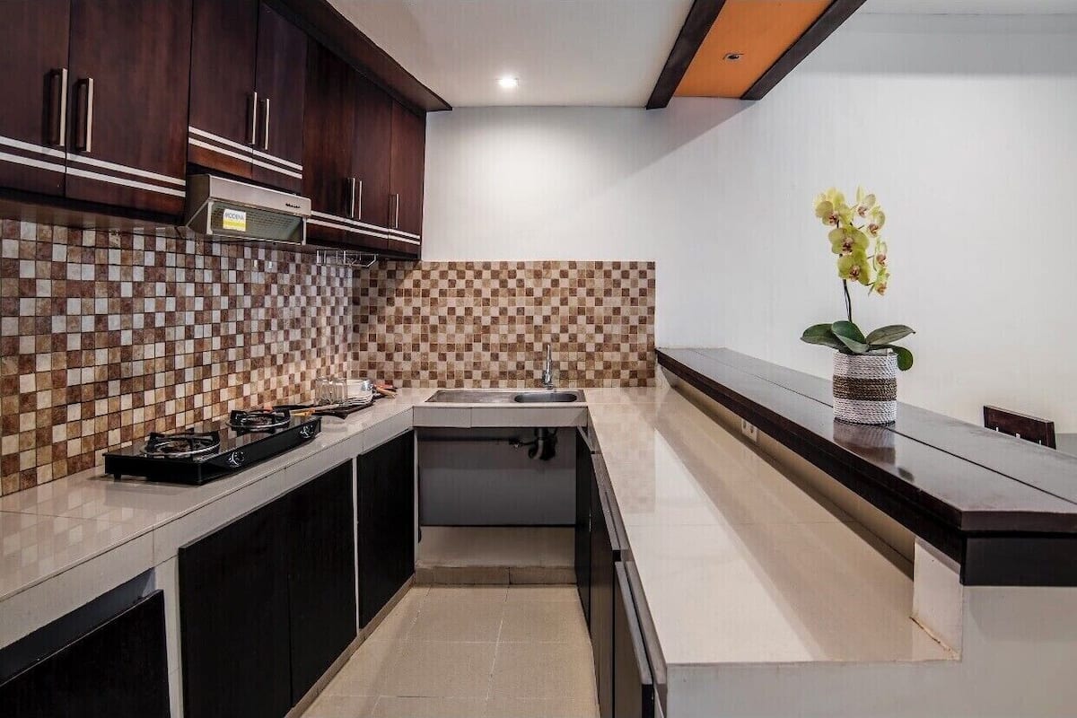 A modern kitchen with dark wooden cabinets, a tiled backsplash, and a central island with a sink.