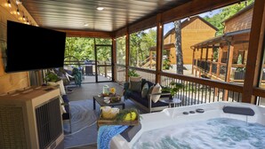 A hot tub on a wooden deck with a TV, seating, and a table with flowers.
