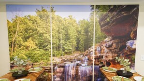 A dining area with a waterfall mural, wooden tables, and green napkins.