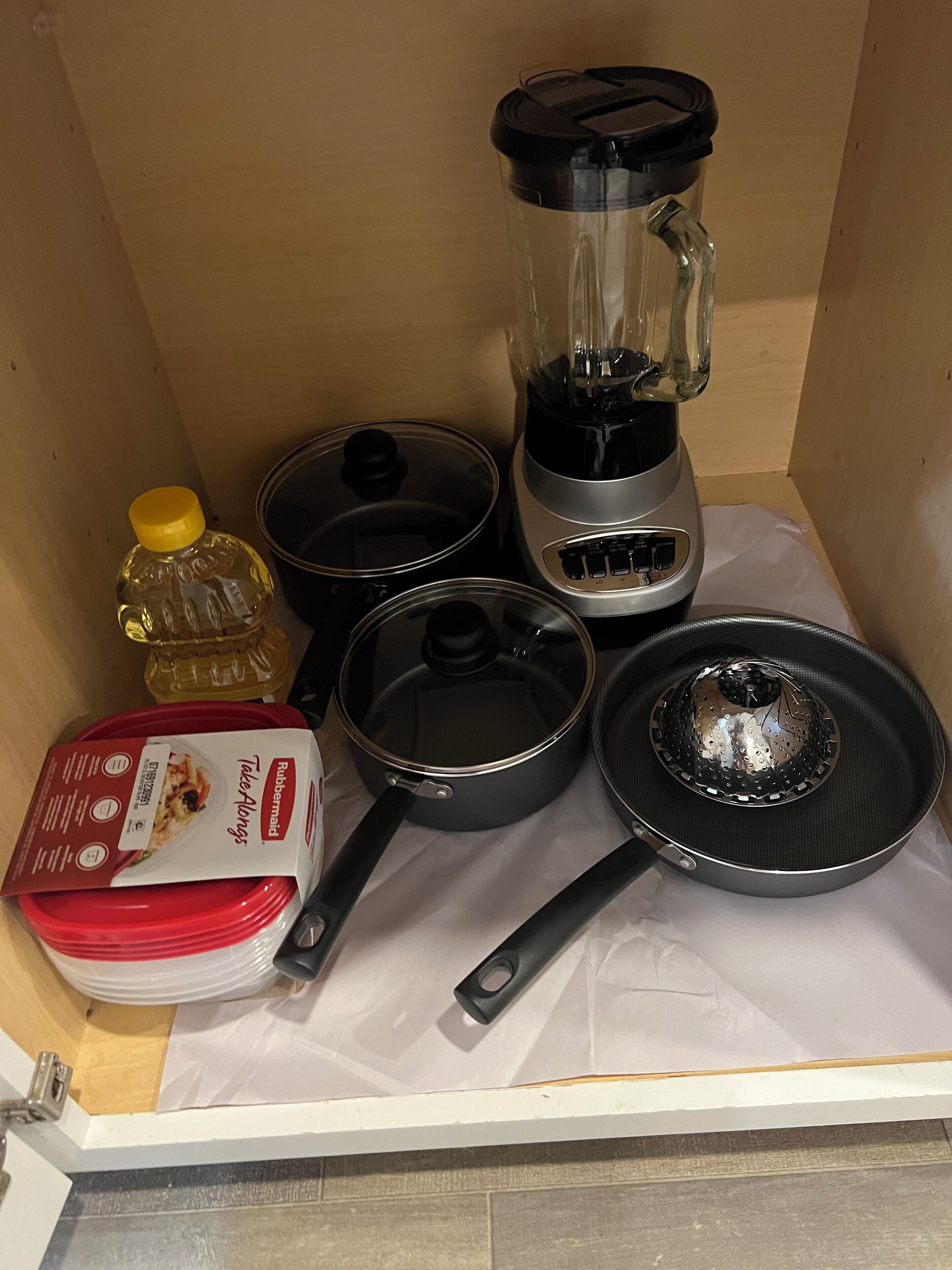 A kitchen area with a blender, two frying pans, a pot, a bottle of cooking oil, and a box of Take Alongs.