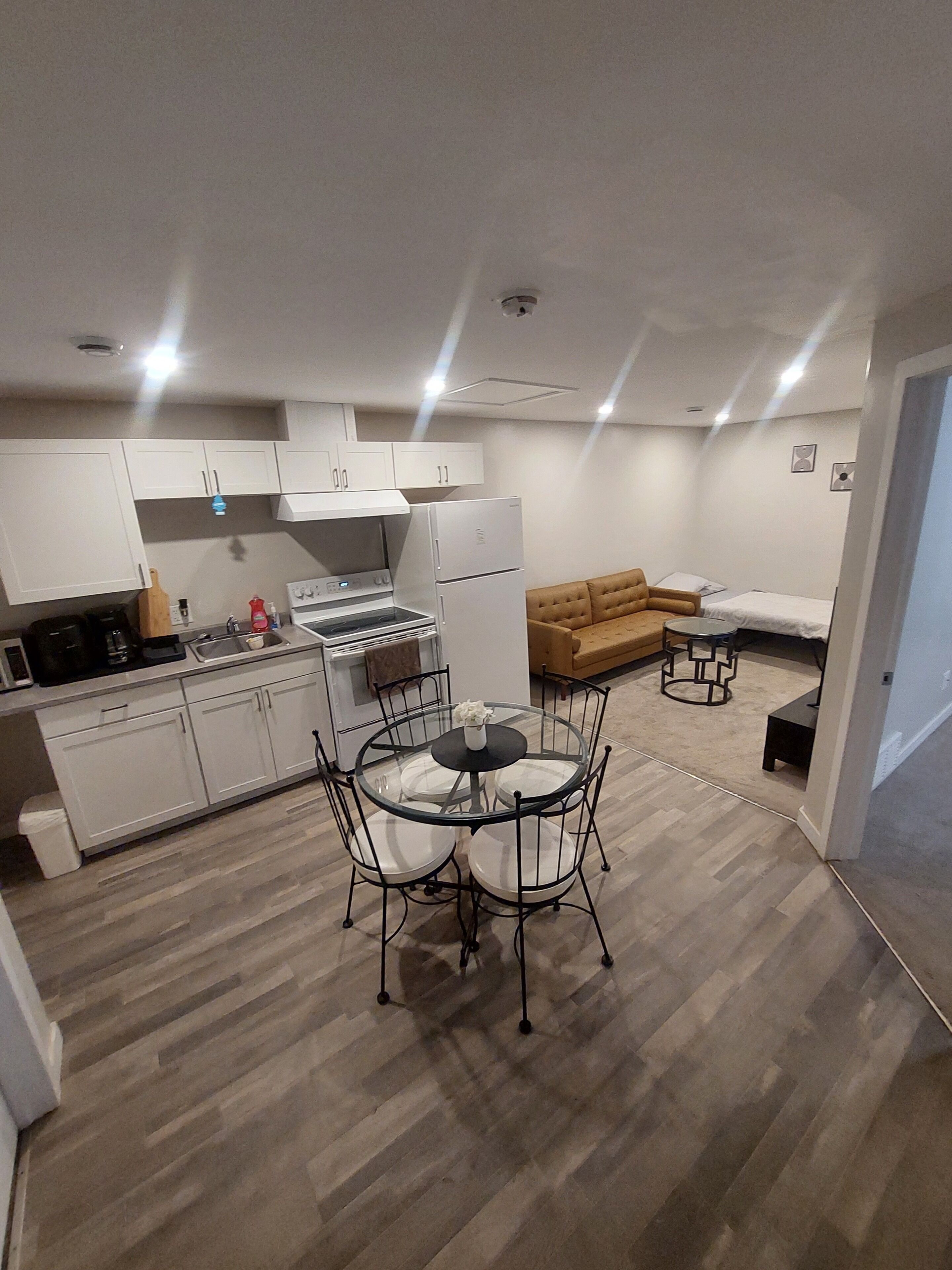 A compact kitchen with white cabinets, a dining table with chairs, a sofa, and a small round table.
