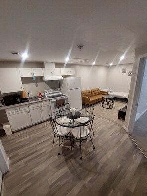A compact kitchen with white cabinets, a dining table with chairs, a sofa, and a small round table. - Private Suite – Private Entrance, Fast Wi‑Fi & Smart TV – Family & Pet‑Friendly (Regina)