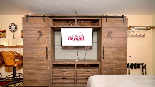 Un dormitorio con una cama, un armario de madera con una pantalla de televisión, una silla y un perchero.