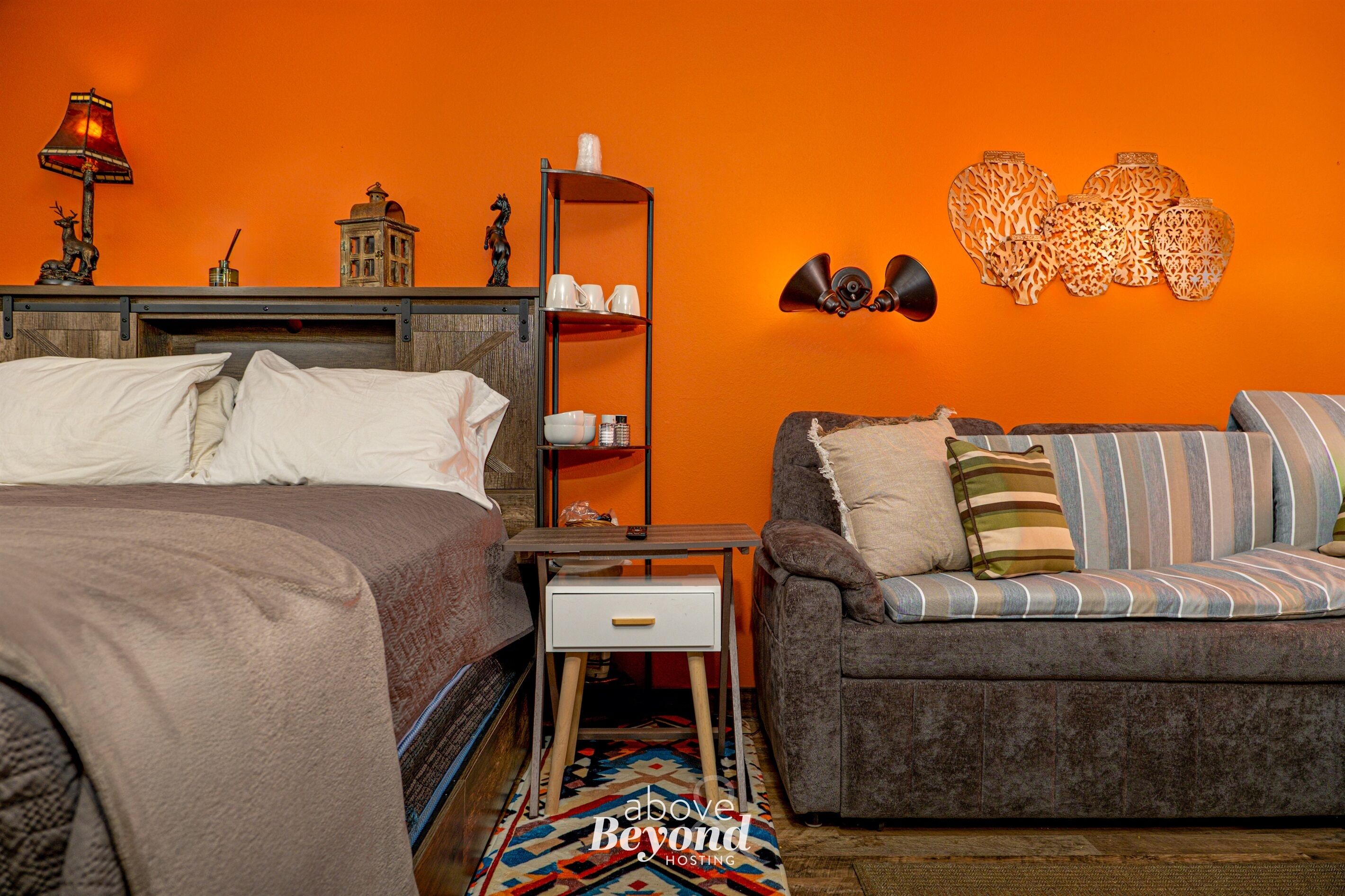 A bedroom with a bed, a sofa, a nightstand, a lamp, and decorative items on the wall.