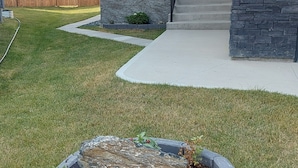Una casa moderna con fachada de piedra, un porche delantero y un jardín ajardinado con flores y acolchado.