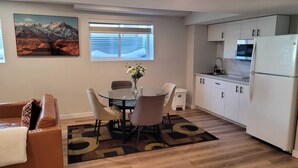 Cocina compacta con armarios blancos, un refrigerador y un microondas. Hay una mesa de comedor con sillas y un jarrón de flores.
