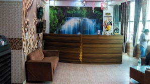 A modern hotel lobby with a reception desk, a sofa, a TV, and a large waterfall mural on the wall. - Hotel Ved & Restaurant  (Agra)