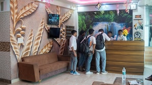 A reception area with a wooden desk, a flat-screen TV, and a wall mural. - Hotel Ved & Restaurant  (Agra)