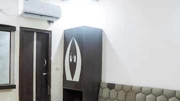 Une chambre avec un plancher en bois, un lit recouvert d’une couvre-lit à motifs floraux, un ventilateur de plafond, un appareil de climatisation et une porte.