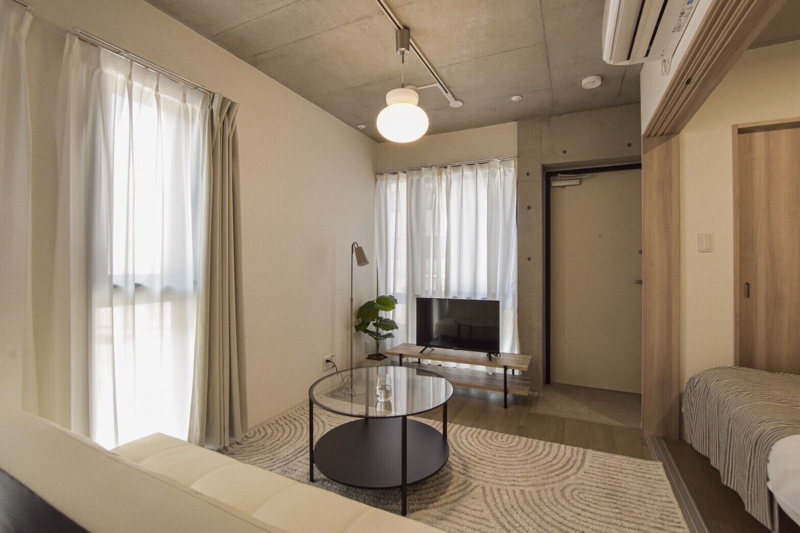 A modern living room with a sofa, a glass coffee table, a TV, and a plant.