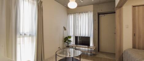 A modern living room with a sofa, a glass coffee table, a TV, and a plant.