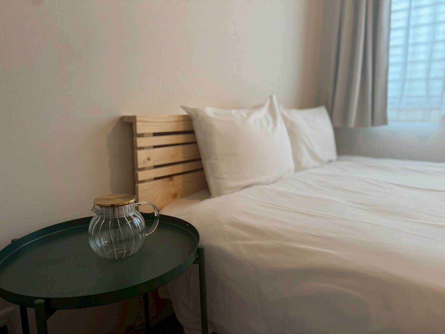 A hotel room with a bed, a small round table with a clear glass pitcher, and a wooden headboard.