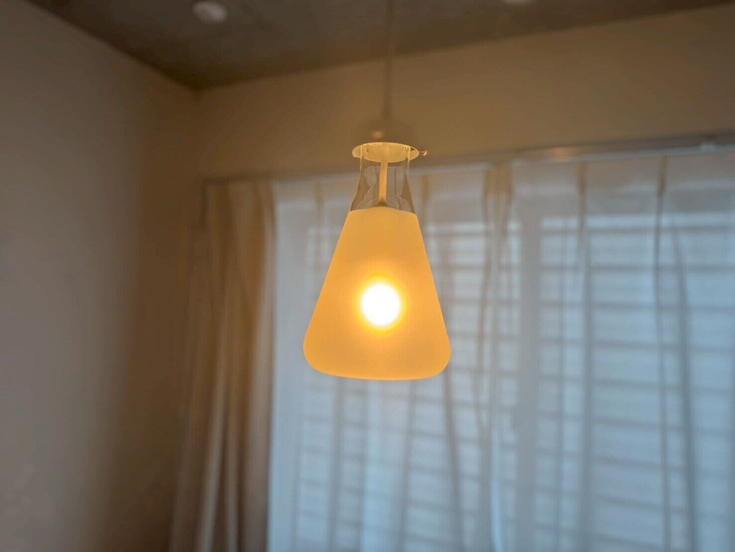 Una lámpara colgante en una habitación con ventana y cortinas.