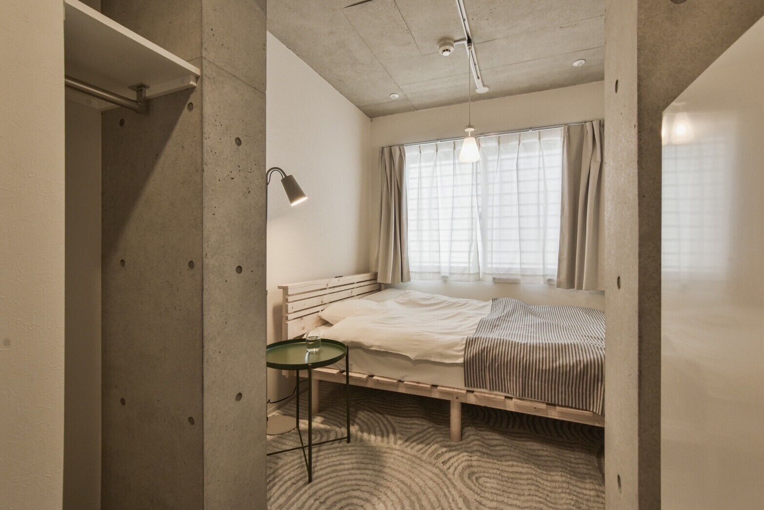 Ein Schlafzimmer mit einem Bett, einem kleinen Tisch, einer Hängelampe und einem Fenster mit Vorhängen.