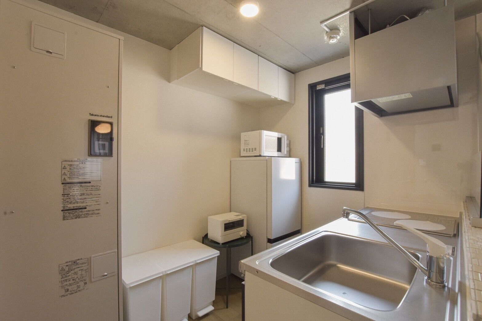 Una cocina compacta con un lavamanos de acero inoxidable, armarios blancos, un microondas y un refrigerador.