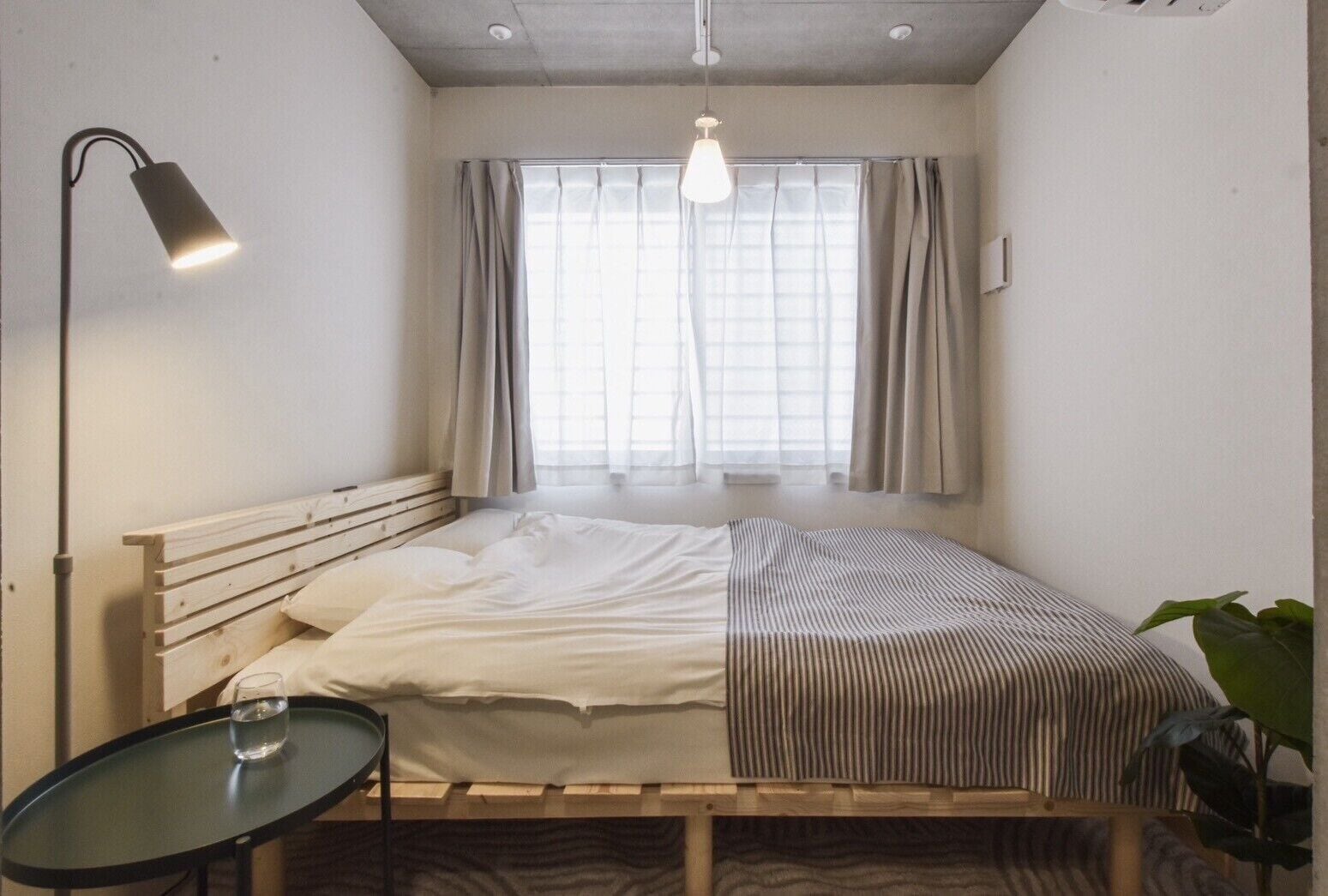 Un lit simple avec une tête de lit en bois, une table de chevet avec un verre et un luminaire suspendu.